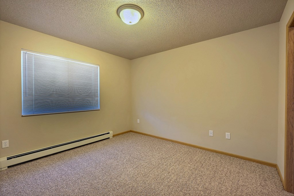 a bedroom with a window and carpet. Fargo, ND East Bridge Apartments
