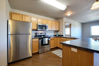 a kitchen with stainless steel appliances and wooden cabinets. Fargo, ND East Bridge Apartments