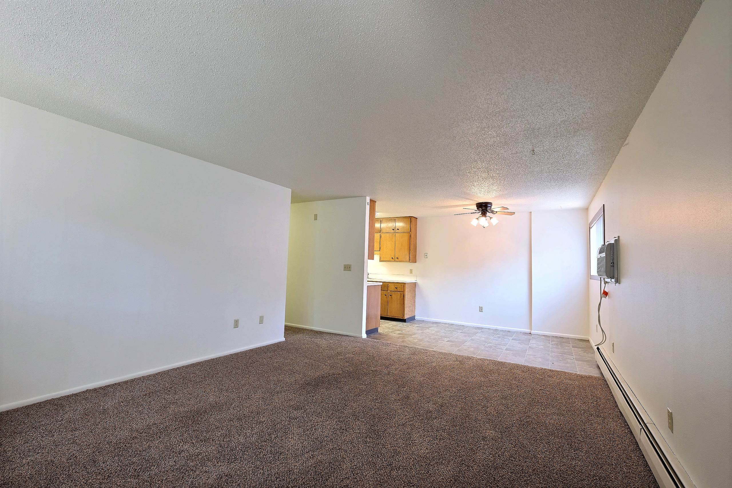 a living room with a kitchen and dining room in the background. Fargo, ND Emerald Apartments