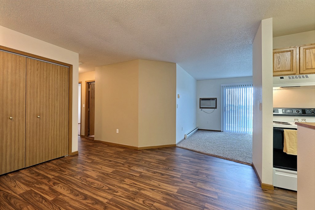 an empty living room and kitchen with wood flooring and a door to the bedroom. Fargo, ND Flagstone Apartments