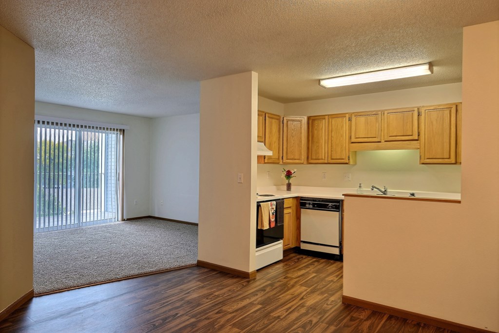 A living room with a glass sliding door and kitchen. Fargo, ND Flagstone Apartments.