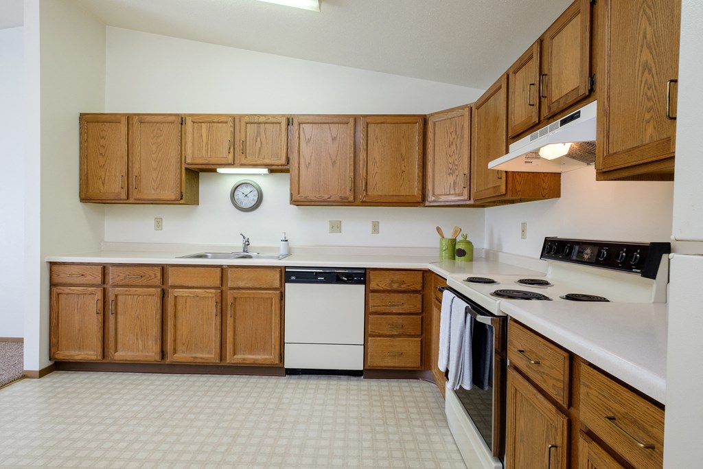an empty kitchen with wooden cabinets and a white counter top. Fargo, ND Flickertail Apartments