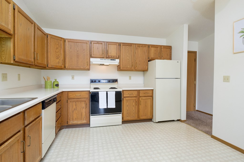 an empty kitchen with white appliances and wooden cabinets. Fargo, ND Flickertail Apartments