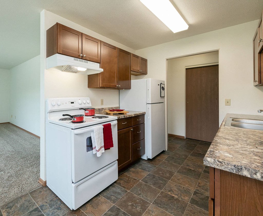 a kitchen with white appliances and wooden cabinets and a white refrigerator. Fargo, ND Islander Apartments