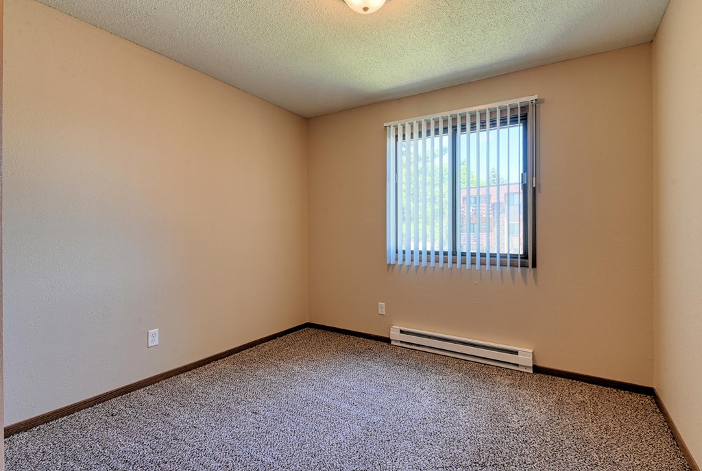 a bedroom with carpeted floors and a window. Grand Forks, ND Madison Apartments