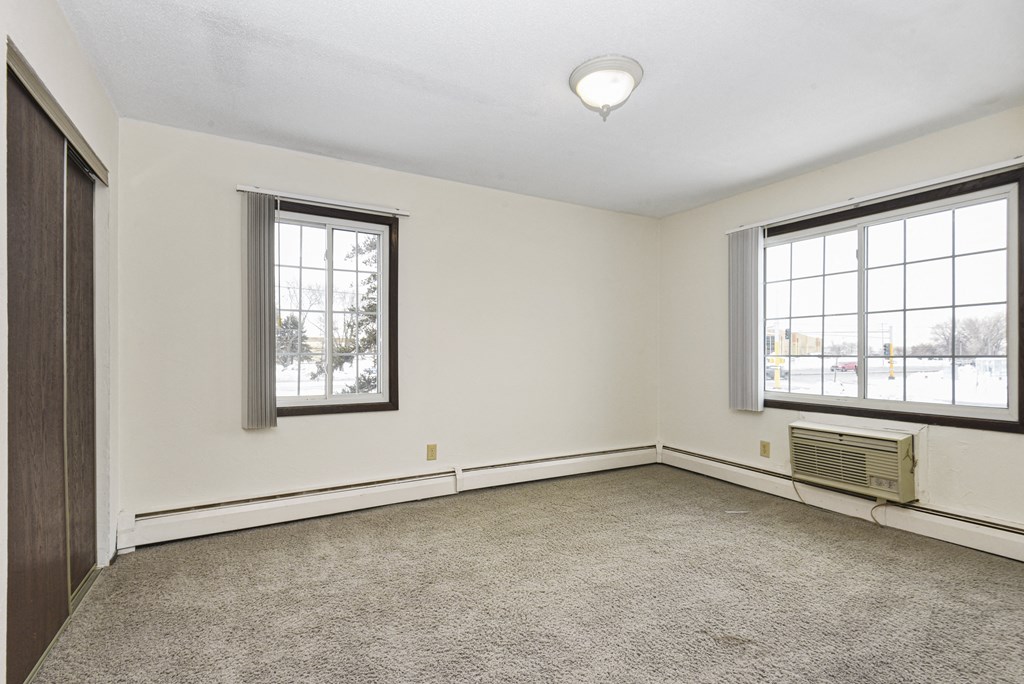 a bedroom of an empty house with carpet and two windows. Fridley, MN Georgetown on the River Apartments