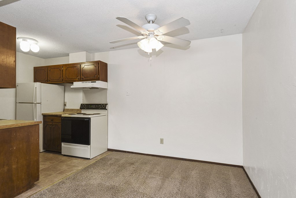 an empty kitchen with a ceiling fan and a white refrigerator. Fridley, MN Georgetown on the River Apartments