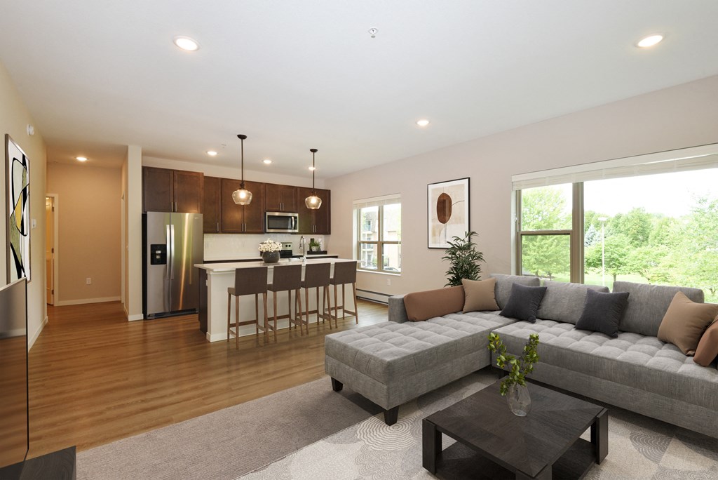 Eagan, MN Glen Pond Addition Apartment. A living room with a couch, coffee table, and large window with a kitchen in the background.