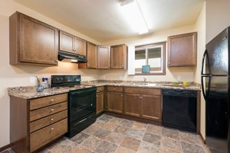 Bismarck, ND Highland Meadows Apartments. a kitchen with brown cabinets and black appliances