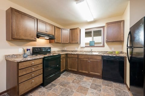 a kitchen with brown cabinets and black appliances at Highland Meadows in Bismarck, ND
