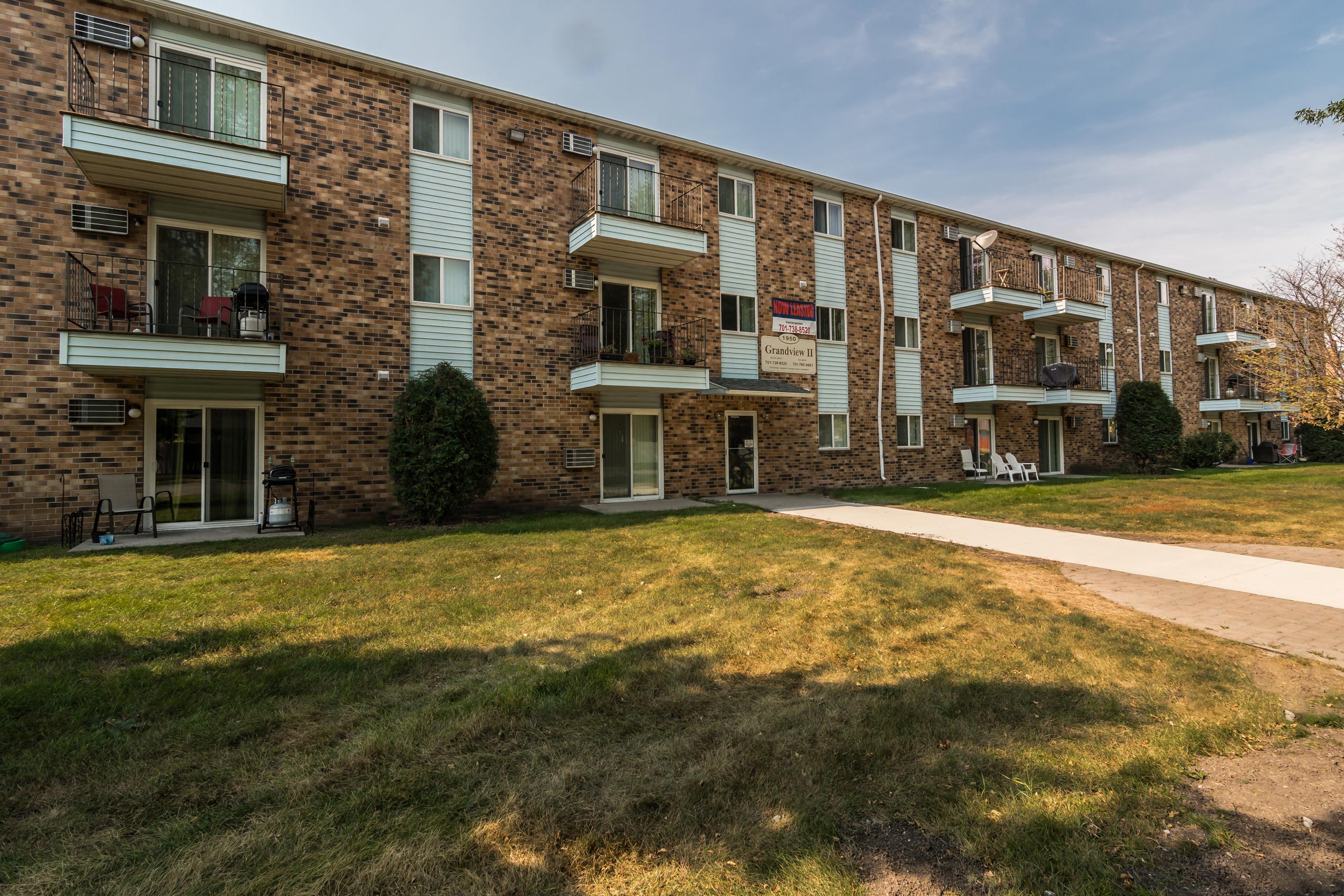 Grand Forks, ND Grandview I Apartments. a brick building with white siding and a grassy area in front of it