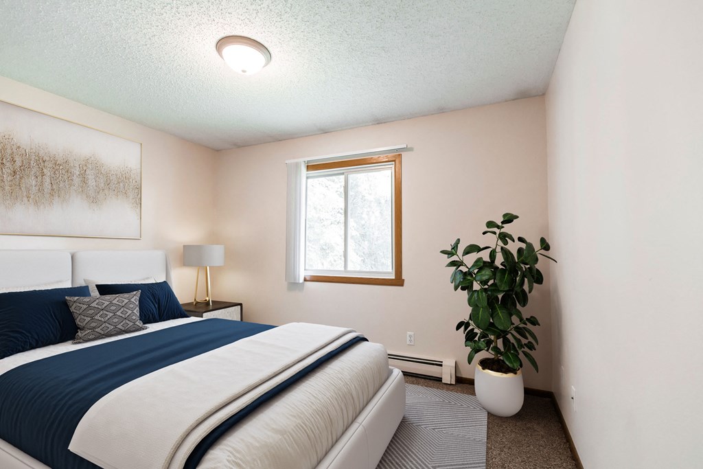a bedroom with a bed and a plant and a window. Bismarck, ND Hannifin Apartments
