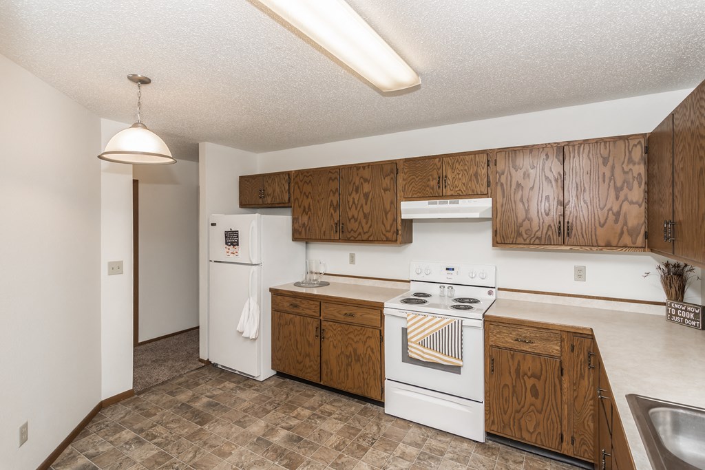 Grand Forks Harrison Apartments. A kitchen with white appliances and wooden cabinets