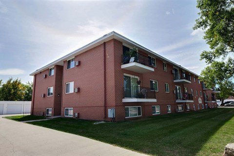 a red brick apartment building with green grass and a sidewalk