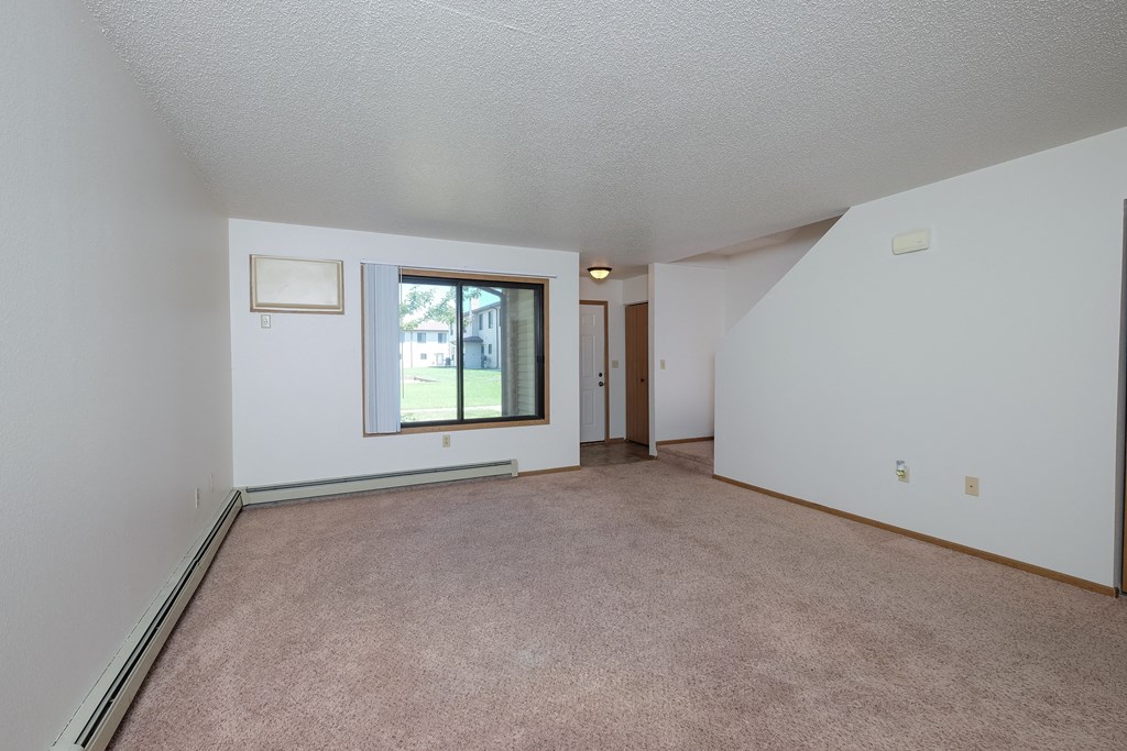 the living room and dining room of an apartment with carpeting and a window. Fargo, ND Hazelwood Townhomes