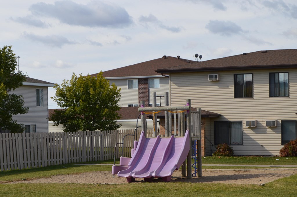 a playground with a set of slides in front of a house. Fargo, ND Hazelwood Townhomes