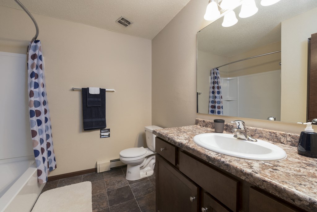 a bathroom with a sink and a toilet and a mirror. Bismarck, ND Highland Meadows Apartments