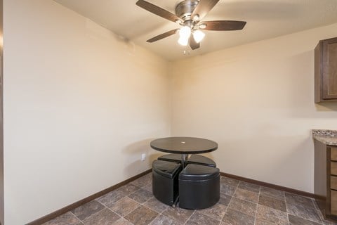 a living room with a ceiling fan and a table with two stools. Bismarck, ND Highland Meadows Apartments