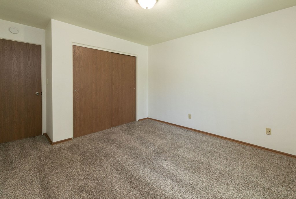 a bedroom with carpet and a door to a closet. Fargo, ND Islander Apartments