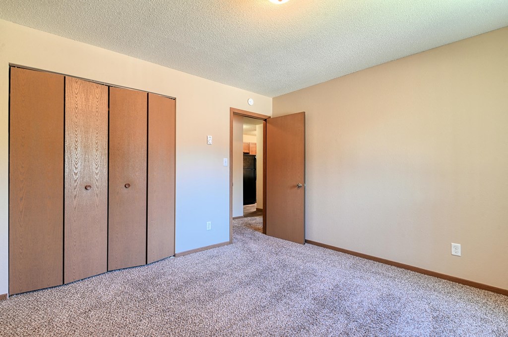 Grand Forks, ND Madison Apartments. A bedroom with a closet and carpeted floors.