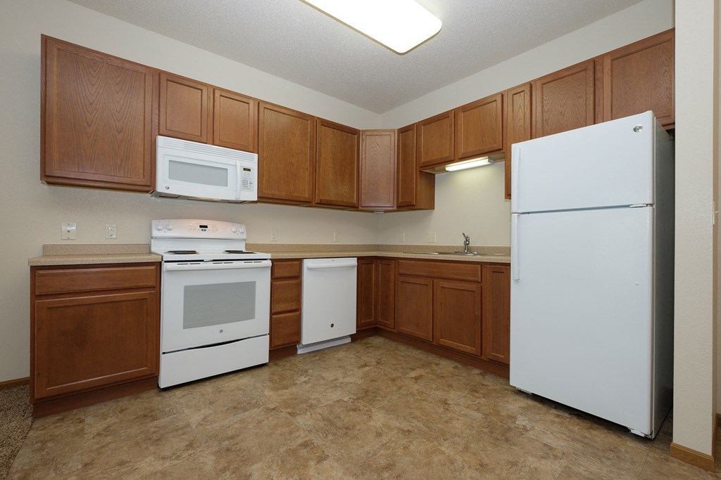 a kitchen with white appliances and wooden cabinets. Fargo, ND North Sky Apartments