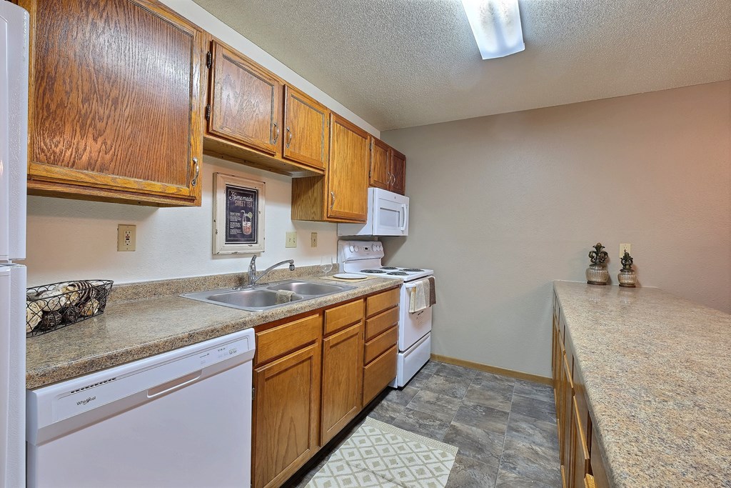 a kitchen with a sink and dishwasher and wooden cabinets. Fargo, ND Kennedy Apartments