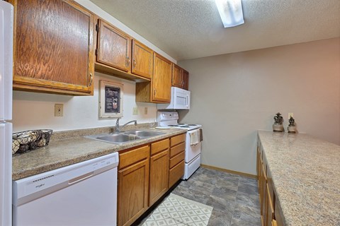 a kitchen with a sink and dishwasher and wooden cabinets. Fargo, ND Kennedy Apartments