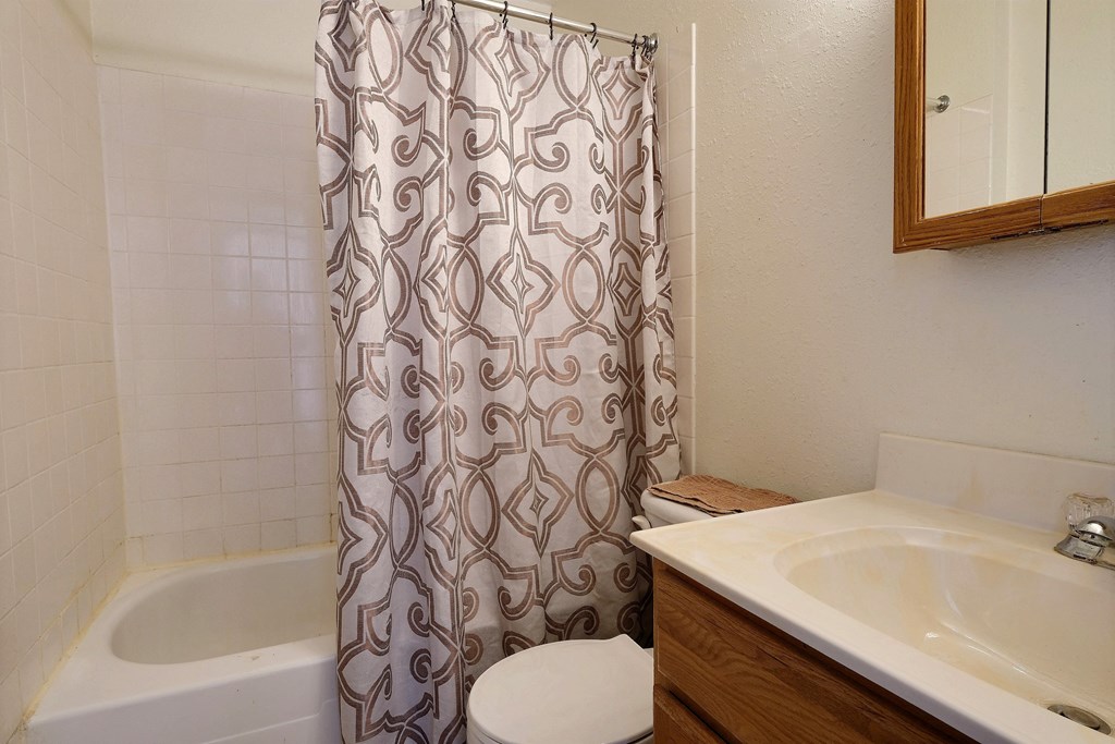 a bathroom with a shower curtain and a sink and a toilet. Fargo, ND Kingswood Apartments