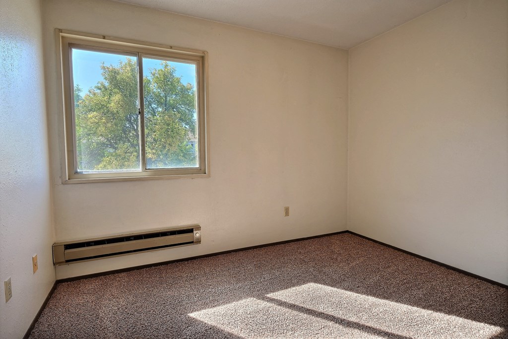 an empty room with a window and carpet. Fargo, ND Kingswood Apartments