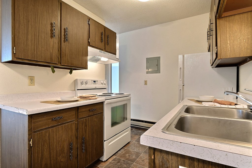 a kitchen with white appliances and wooden cabinets and a sink. Fargo, ND Kingswood Apartments