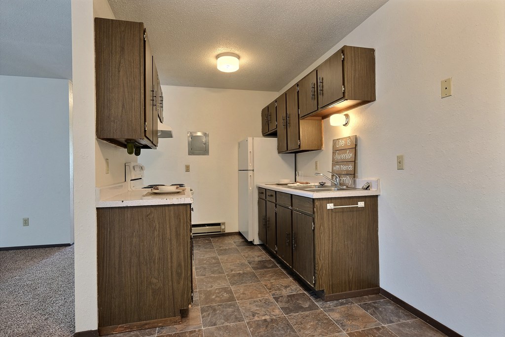 an empty kitchen with wooden cabinets and a refrigerator. Fargo, ND Kingswood Apartments