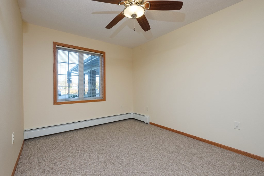 a bedroom with a window and a carpeted floor. Fargo, ND Crossroads Apartments