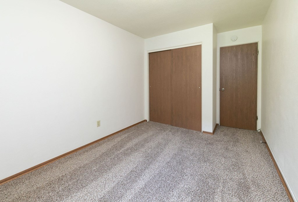 a room with a carpeted floor and a wooden door. Fargo, ND Islander Apartments