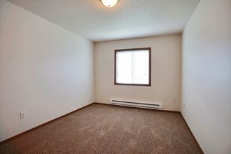A bedroom of apartment with carpet and a window. Fargo, ND Lake Crest Apartments.
