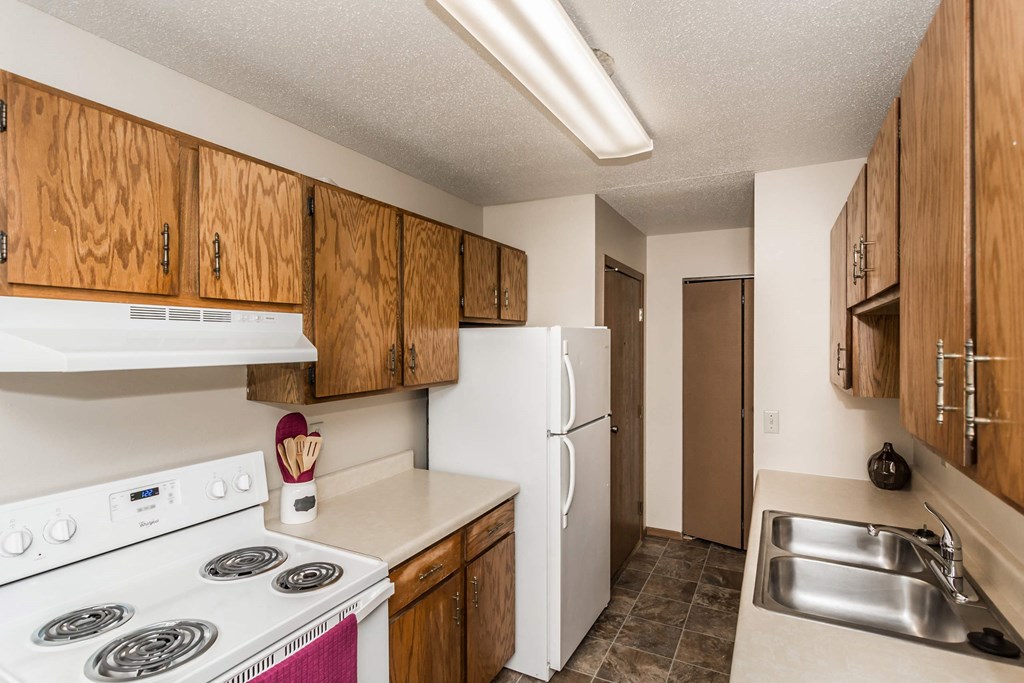 Grand Forks, ND Library Lane Apartments. A kitchen with a white refrigerator freezer next to a stove top oven