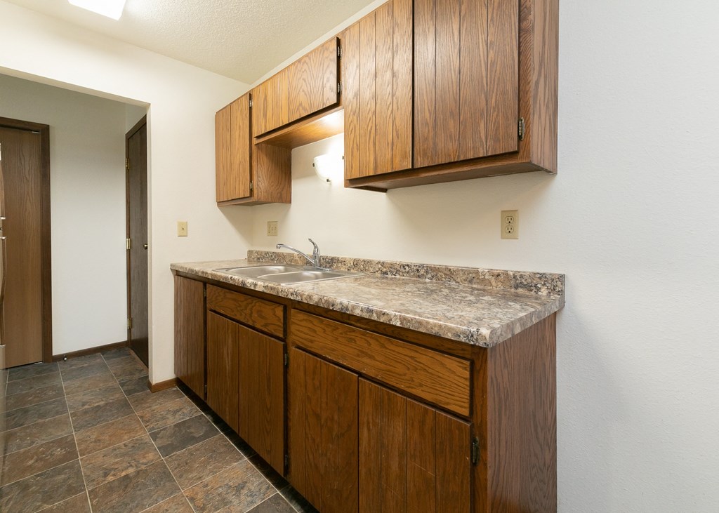 a kitchen with a sink and cabinets and a door to a hallway .Fargo, ND Maplewood Bend Apartments