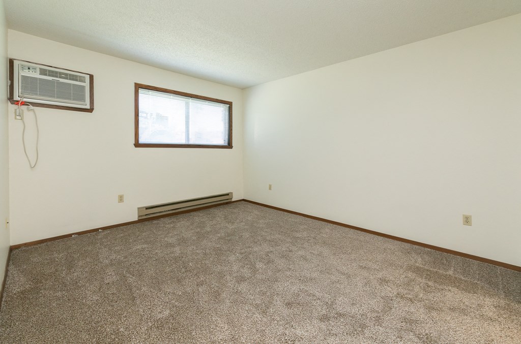 an empty living room with carpet and a window .Fargo, ND Maplewood Bend Apartment