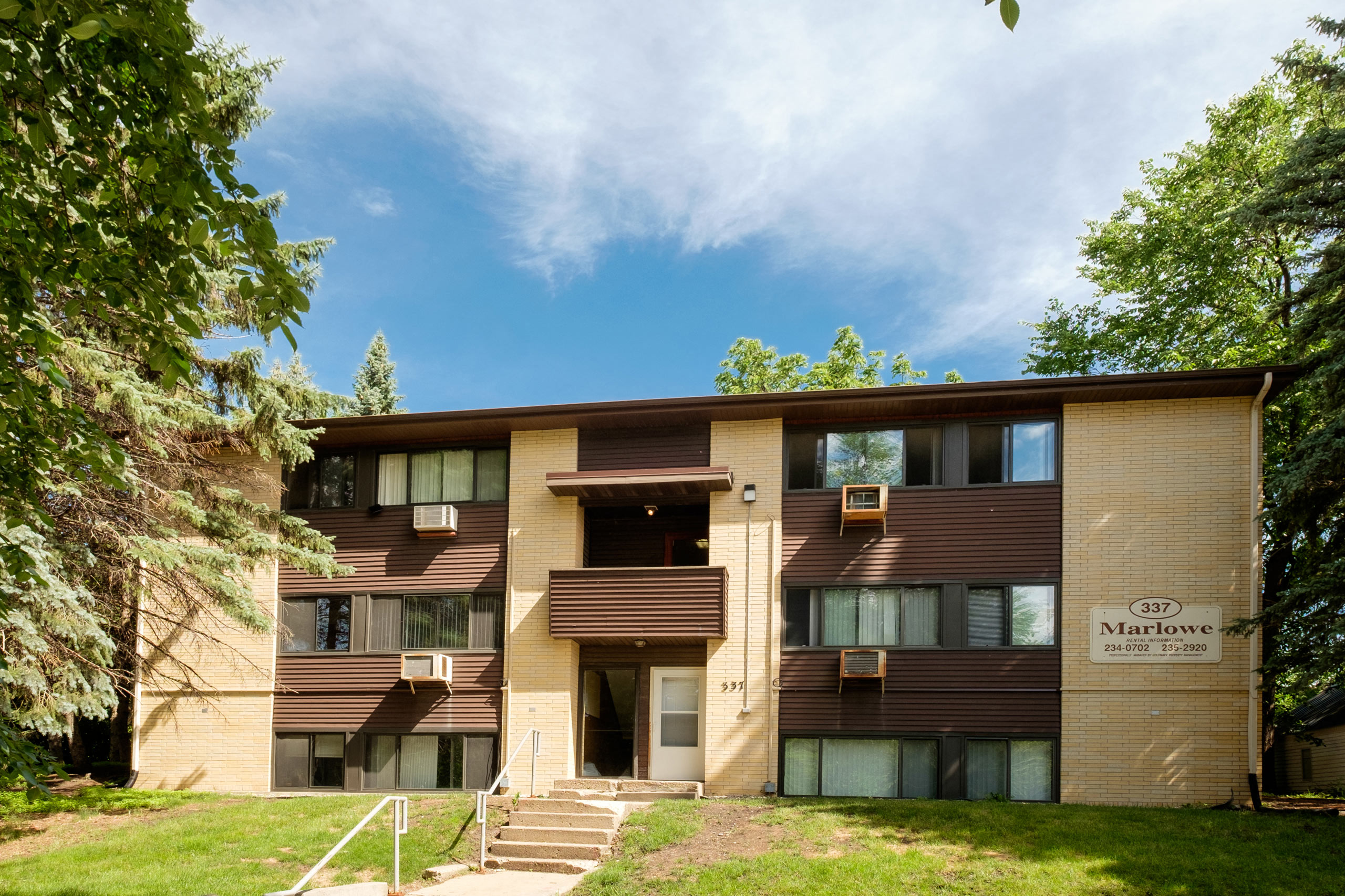 a brown apartment building with trees and a blue sky