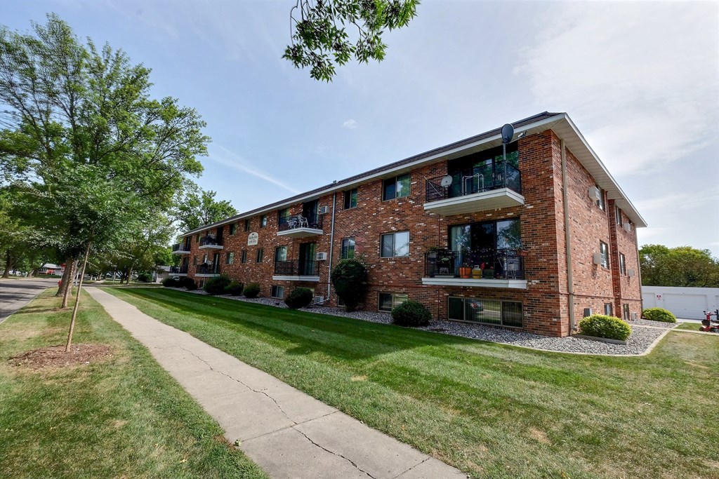 the exterior of a brick apartment building with a sidewalk and grass. Fargo, ND Martha Alice Apartments