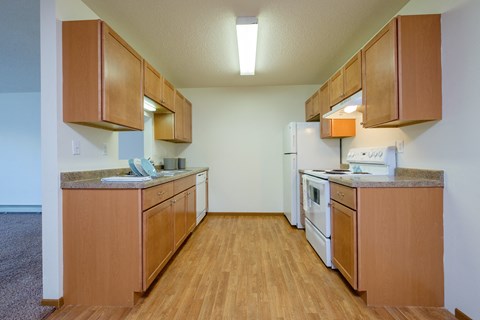 an empty kitchen with wooden cabinets and white appliances. Fargo, ND Maybrook Apartments