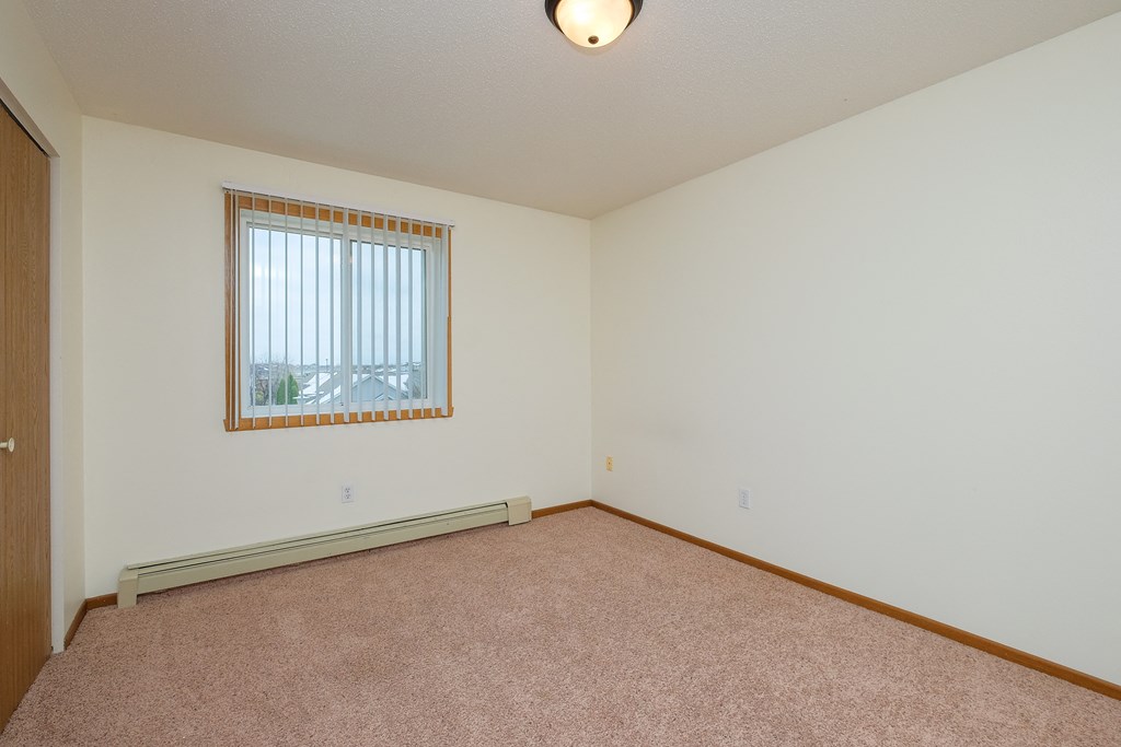 a bedroom with carpet and a window. Fargo, ND Maybrook Apartments