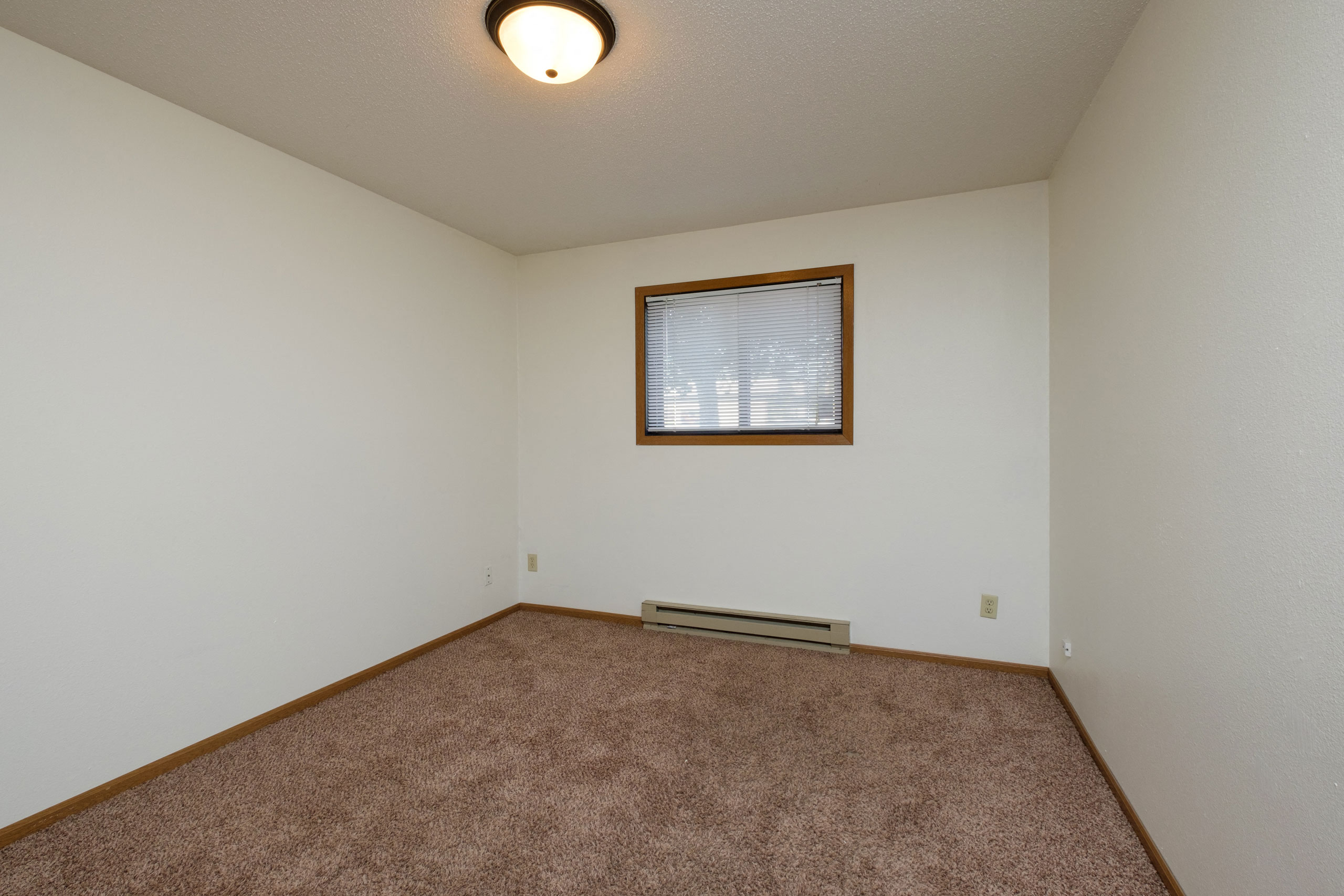 a bedroom with carpeted floors and a window. Fargo, ND Monticello Apartments