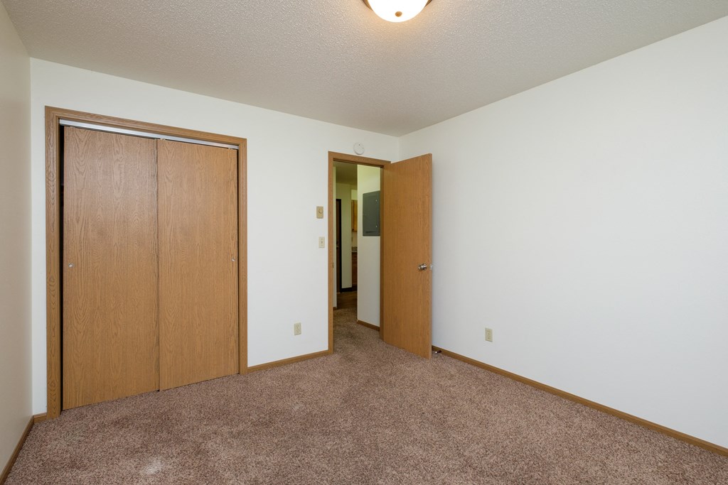 a bedroom with a carpeted floor and a door to a closet. Fargo, ND Monticello Apartments