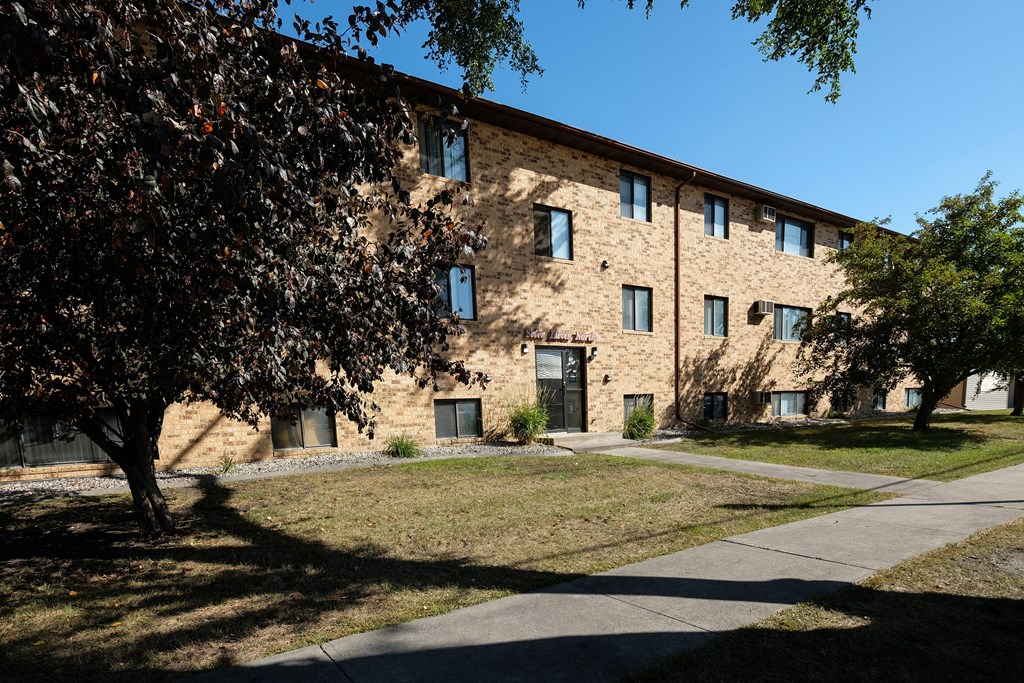 a brick building with a sidewalk and trees in front of it. Fargo, ND Monticello Apartments