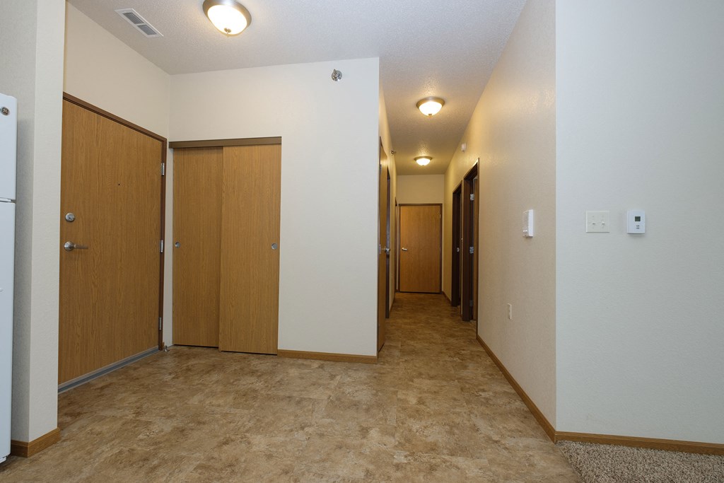 a hallway with white walls and wooden doors and a carpeted floor. Fargo, ND North Sky Apartments