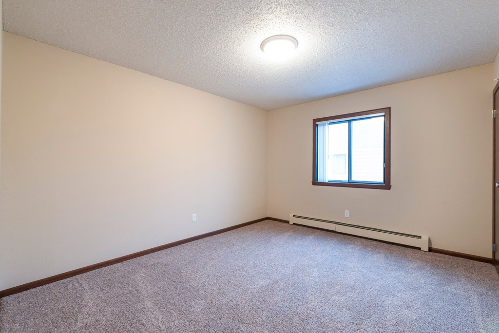 a bedroom with carpet and a window. Bismarck, ND Newgate Apartments