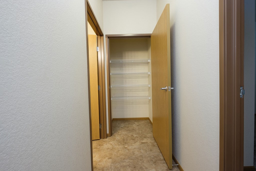 a hallway with a closet with shelves and a door open. Fargo, ND North Sky Apartments