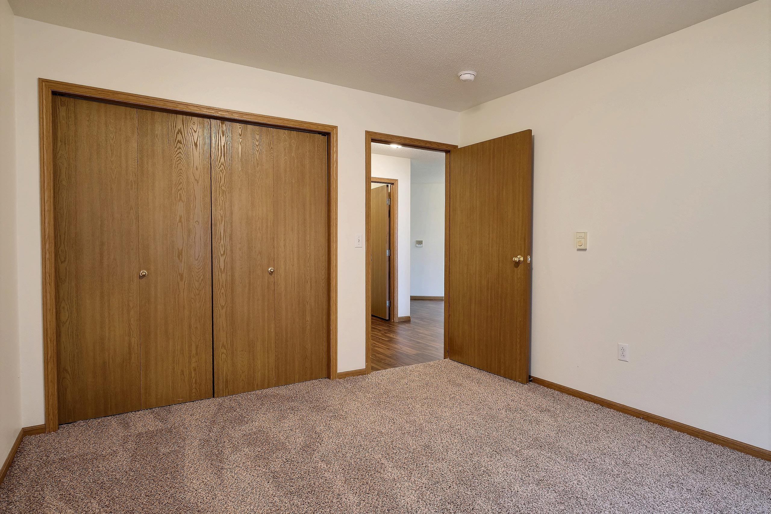 A bedroom with a closet and a door to a hallway. Fargo, ND Oxford Apartments.