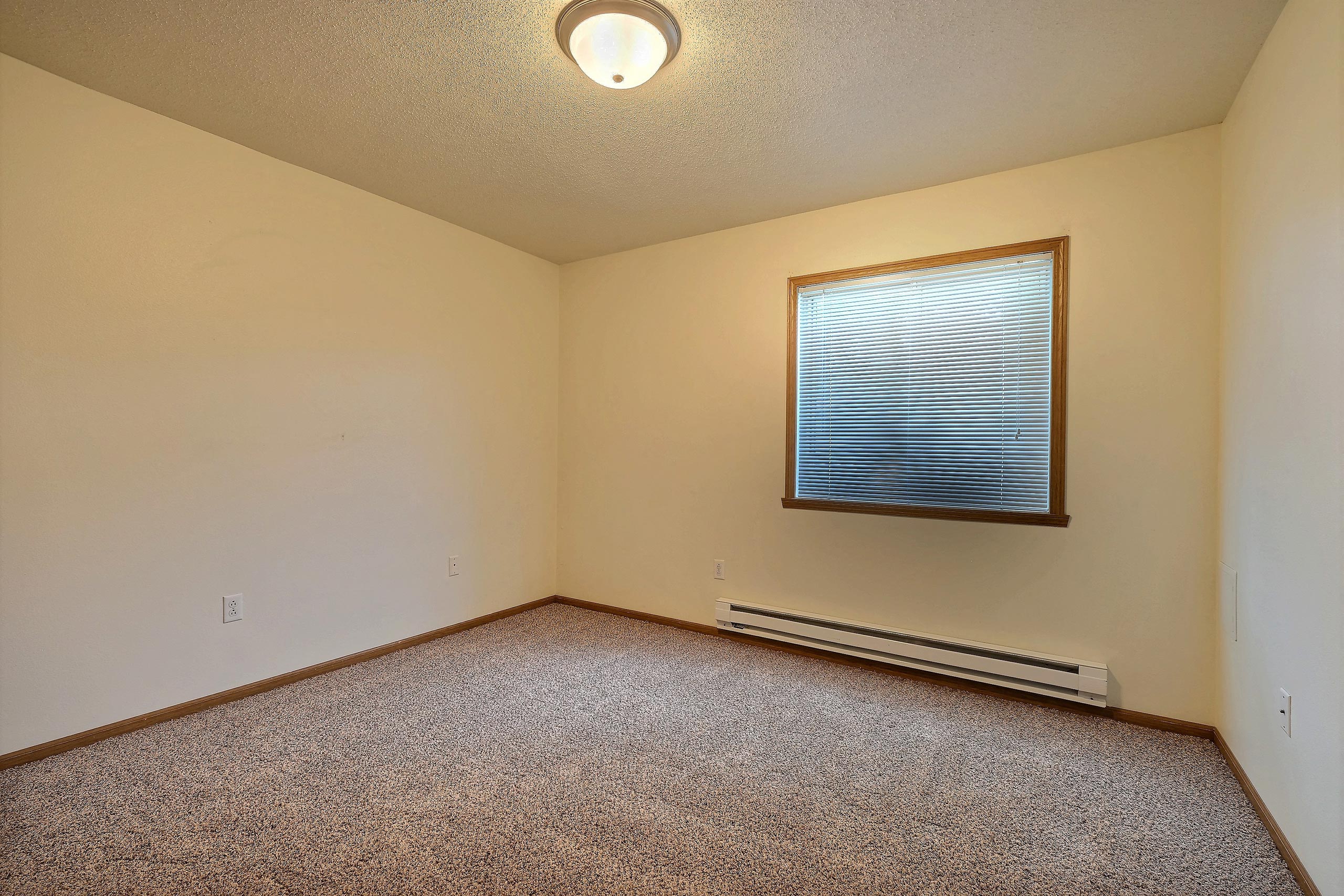 A bedroom with a window and baseboard heater. Fargo, ND Oxford Apartments.