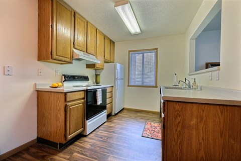 A kitchen with white appliances and wooden cabinets. Fargo, ND Oxford Apartments.